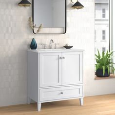 a white bathroom vanity with two lights and a mirror on the wall next to a potted plant