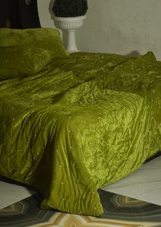 a bed with green bedspread and pillows on top of it next to a potted plant