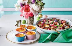 a table topped with plates and bowls filled with food next to a vase full of flowers