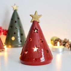 three small christmas trees with lit candles in front of them on a white table top