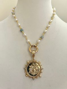 An elegant pearl and aqua stone rosary chain necklace with gold wire and a French Le Monde replica coin pendant. The pendant hangs off a beautiful thick gold bale. The coin bezel, an Art Deco French stunner has Clear CZ and Pearl accents. The clasp is a spring ring and so easy to handle. Please see the picture of the clasp opening. Material: Bezel is made of Cast Zinc Alloy and the coin is of brass Measure - Bezel and coin = 40mm Coin = 28mm Spring ring =20mm Tips to keep your jewelry looking go Gold Medallion Jewelry With Pearl Charm, Gold Pearl Jewelry With Coin Pendant, Gold Pearl Necklace With Coin Pendant, Gold Coin Necklace With Pearl Chain, Gold Medallion Pearl Necklace With Pendant, Gold Pearl Pendant Necklace In Medallion Shape, Gold Pearl Necklace With Medallion Pendant, Gold Medallion Jewelry With Pearl Chain, Rosary Chain Necklace