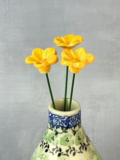 three yellow flowers in a blue and white vase on a table with grey background,