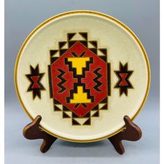 a white plate with red, yellow and black designs on the front sitting on a wooden stand