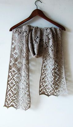 an openwork shawl hanging on a wooden hanger against a white wall,