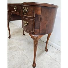 a wooden desk with two drawers and gold hardware on the top, against a white wall