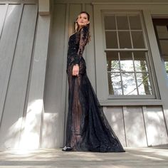 a woman in a long black dress standing on a porch next to a building with windows