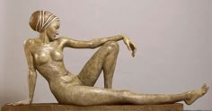 a bronze statue sitting on top of a wooden table next to a white wall and floor