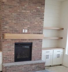 an empty living room with a brick fireplace and built - in shelving units on either side