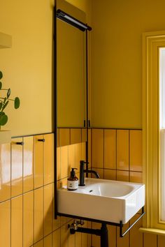 a white sink sitting under a bathroom mirror next to a yellow tiled wall with a potted plant