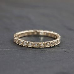 a gold wedding band with five diamonds on it, sitting on a black stone surface