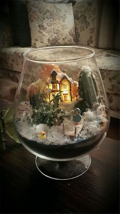 a glass bowl filled with snow and a house in the center, on top of a wooden table