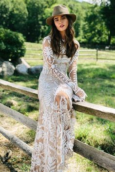 a woman in a white dress and hat sitting on a fence