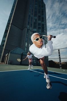 an older woman is playing tennis on the court in front of a tall building with many windows