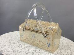 "Vintage 1950s Lucite Purse Circa - 1950s Label - N/A Color - Clear white pink blue Material - Lucite lace hand painting DETAILS - - rare style - 2 clear  top handles - box style  - lace insertion with hand painted flowers - top opening on brass hinged top - great gift idea PJ482 MEASUREMENTS - width - 6\" depth - 3.5\" length w/o handles - 6.5\" length with handles - 9\" CONDITION - excellent *Visit shop -https://www.etsy.com/shop/LadyScarlettsVintage?ref=seller-platform-mcnav *VFG member" Lace Insertion, Lucite Purse, Painting Details, Clear Top, Brass Hinges, Dog Bones, Hand Painted Flowers, Painted Flowers, Clear White