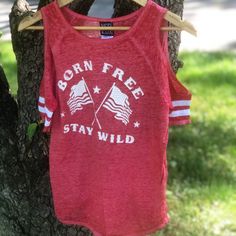 a red shirt hanging from a tree with the words born free stay wild on it