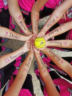 a group of girls in pink shirts holding a yellow ball with writing on their arms