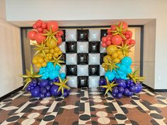 balloons and streamers are arranged on the floor in front of a checkerboard backdrop