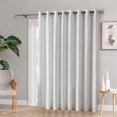 a living room with white curtains and a plant in front of the sliding glass door