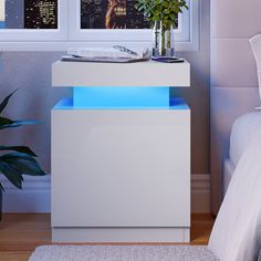 a white nightstand with blue lights on it next to a bed and potted plant