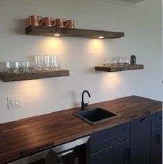 the kitchen counter is made from wood and has two shelves above it with glasses on them