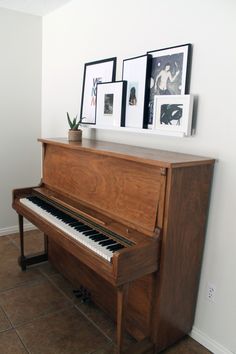 a wooden piano sitting on top of a tile floor next to a white wall and framed pictures