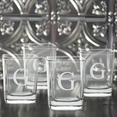 three glasses with the letter g on them are sitting on a table next to each other