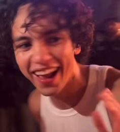 a man with curly hair is smiling and making the peace sign while holding his hand up in front of him