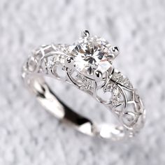 a white gold engagement ring with an intricate design and round brilliant cut diamond in the center