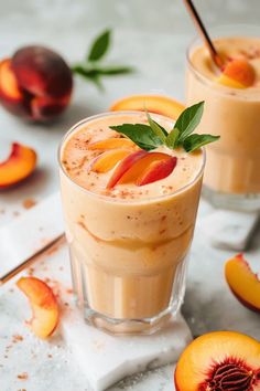 two glasses filled with peach smoothie and garnished with fresh fruit on the side