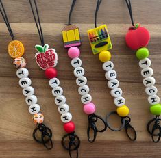 four different key chains with fruit and letters on them sitting on top of a wooden table