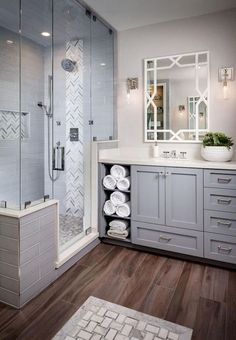 a bathroom with gray cabinets and white towels on the counter, along with a walk in shower