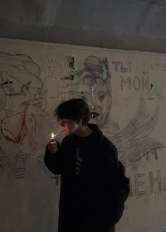 a young boy holding a lit candle in front of a wall with drawings on it