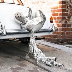 balloons tied to the back of a white car with silver foil on it's tail