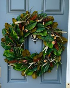 a wreath is hanging on the front door with green leaves and other greenery around it