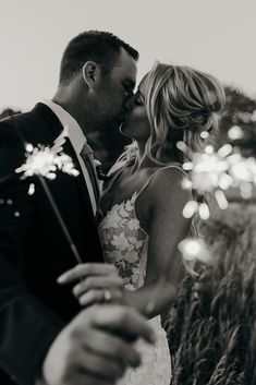 a bride and groom kissing in front of sparklers at their wedding reception, black and white photo