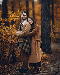 a man and woman are hugging in the woods with autumn leaves around them, while they stand close to each other