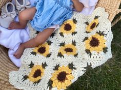 a baby laying in a basket with sunflowers on the ground next to it