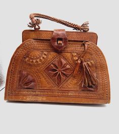 A beautiful and unique handbag with a woven top handle in honey-colored leather, vintage 70s. The surface on this is completely engraved by hand with geometric and ornamental motifs. The closure is very special.  There is some wear to this purse, as seen in photos. This is to be expected for a bag of this age. The structure is solid. Please see all photos for details.  Measures: Drop of purse handle: 5" Height: 10" Length: 14" Width: 4"  Happy to bundle, please reach out.  Ships securely package Vintage Embossed Satchel For Everyday Use, Vintage Bag With Leather Handles, Vintage Rectangular Bag With Leather Handles, Vintage Bag With Leather Handles And Rectangular Shape, Vintage Brown Embossed Satchel, Vintage Embossed Satchel Bag, Vintage Brown Embossed Shoulder Bag, Vintage Brown Bag With Leather Handles, Traditional Brown Formal Bag