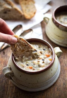 a hand holding a piece of bread over a bowl of soup