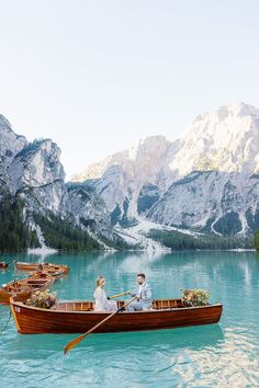 two people sitting in a boat on the water with mountains in the backgroud