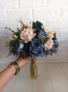 a person holding a bouquet of blue and pink flowers in front of a white brick wall