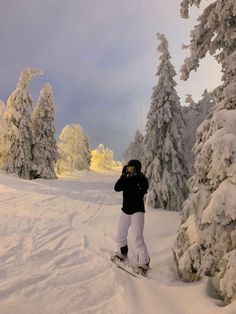 a man riding skis down a snow covered slope next to tall pine tree's