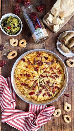 a pizza sitting on top of a wooden table next to other foods and condiments