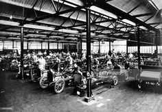 an old factory with many cars and people working on the assembly line in front of them