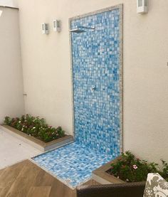 an outdoor shower with blue tiles on the wall and flowers in pots next to it