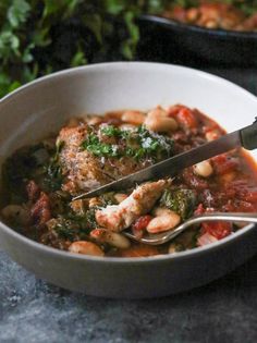 a white bowl filled with meat and beans next to a green leafy plant in the background