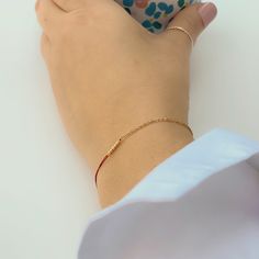 Close-up of hand wearing delicate bracelet of gold chain and red thread with gold beads detail at center. Everyday Tiny Beads Chain Bracelet, Minimalist Yellow Gold Beaded Chain Bracelet, Gold Beaded Chain Friendship Bracelets As Gift, Minimalist Beaded Chain Bracelet, Yellow Gold Minimalist Bracelet For Parties, Minimalist Yellow Gold Bracelet For Party, Minimalist Yellow Gold Party Bracelet, Party Minimalist Yellow Gold Bracelet, Minimalist Chain Bracelet For Party