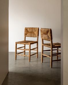 two wooden chairs sitting next to each other on a cement floor in front of a white wall