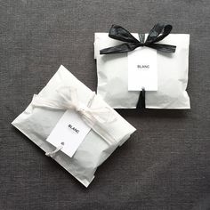 two wrapped gift bags with black ribbon and white paper tags tied around them on a gray surface