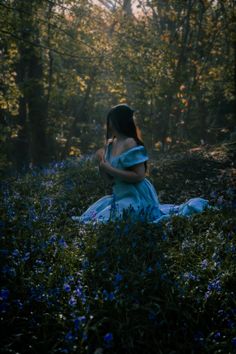 a woman in a blue dress is sitting on the ground surrounded by flowers and trees